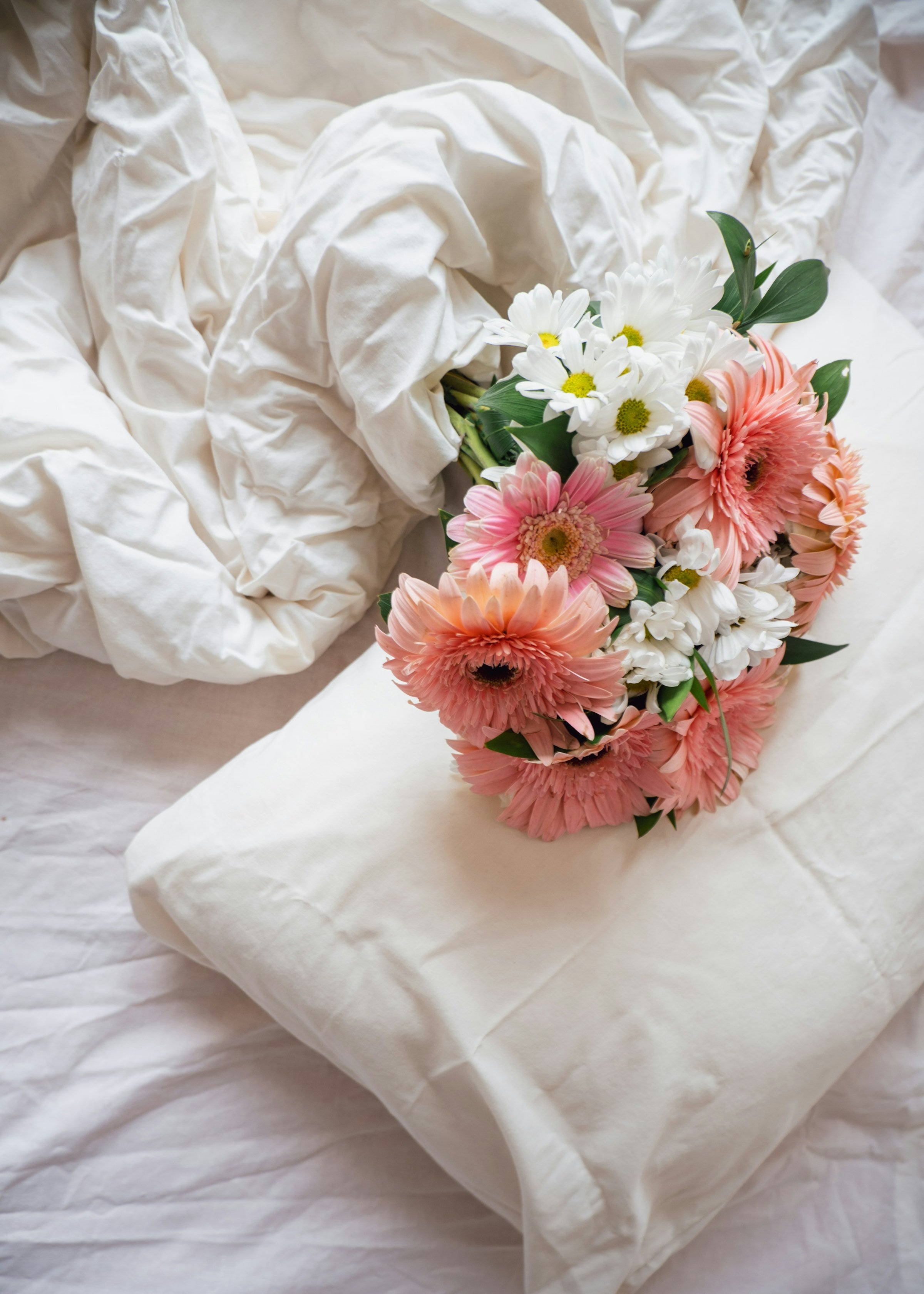 Bouquet of pink and white flowers on a white pillow with white bedding