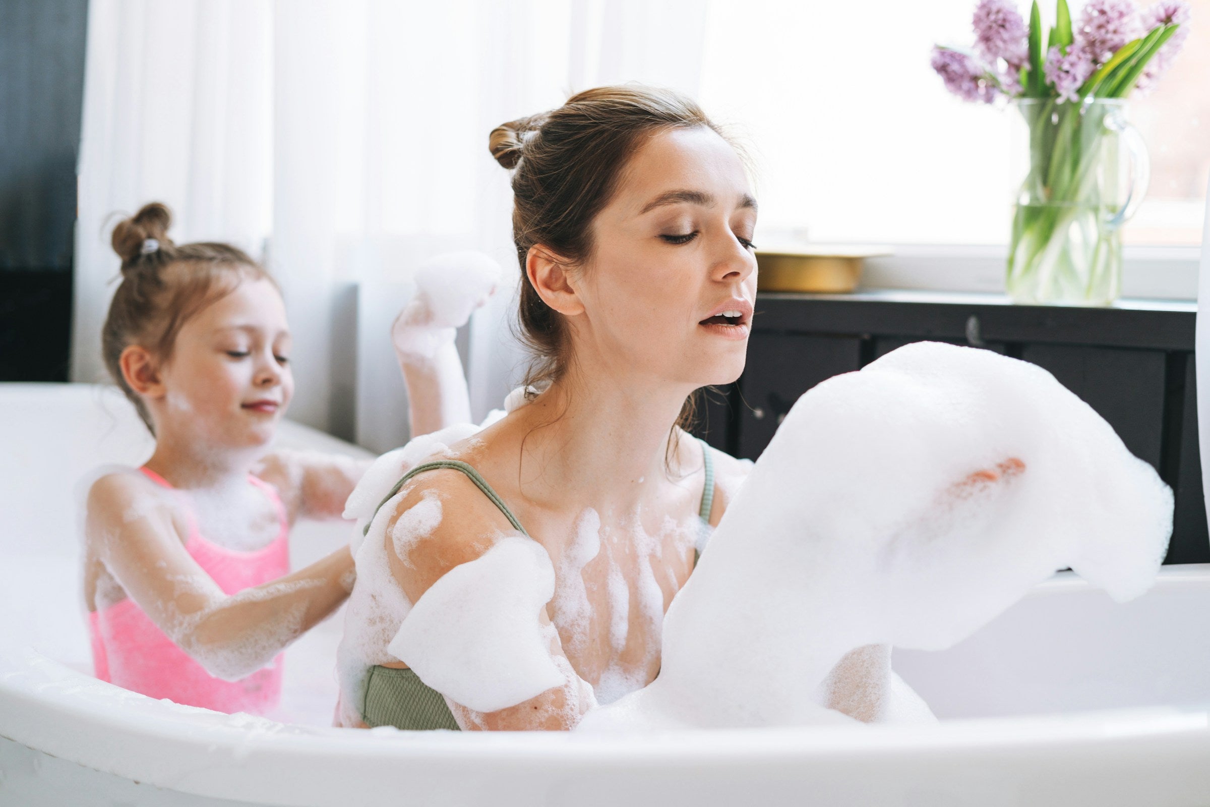 Woman and child in a bubble bath with a vase of flowers in the background