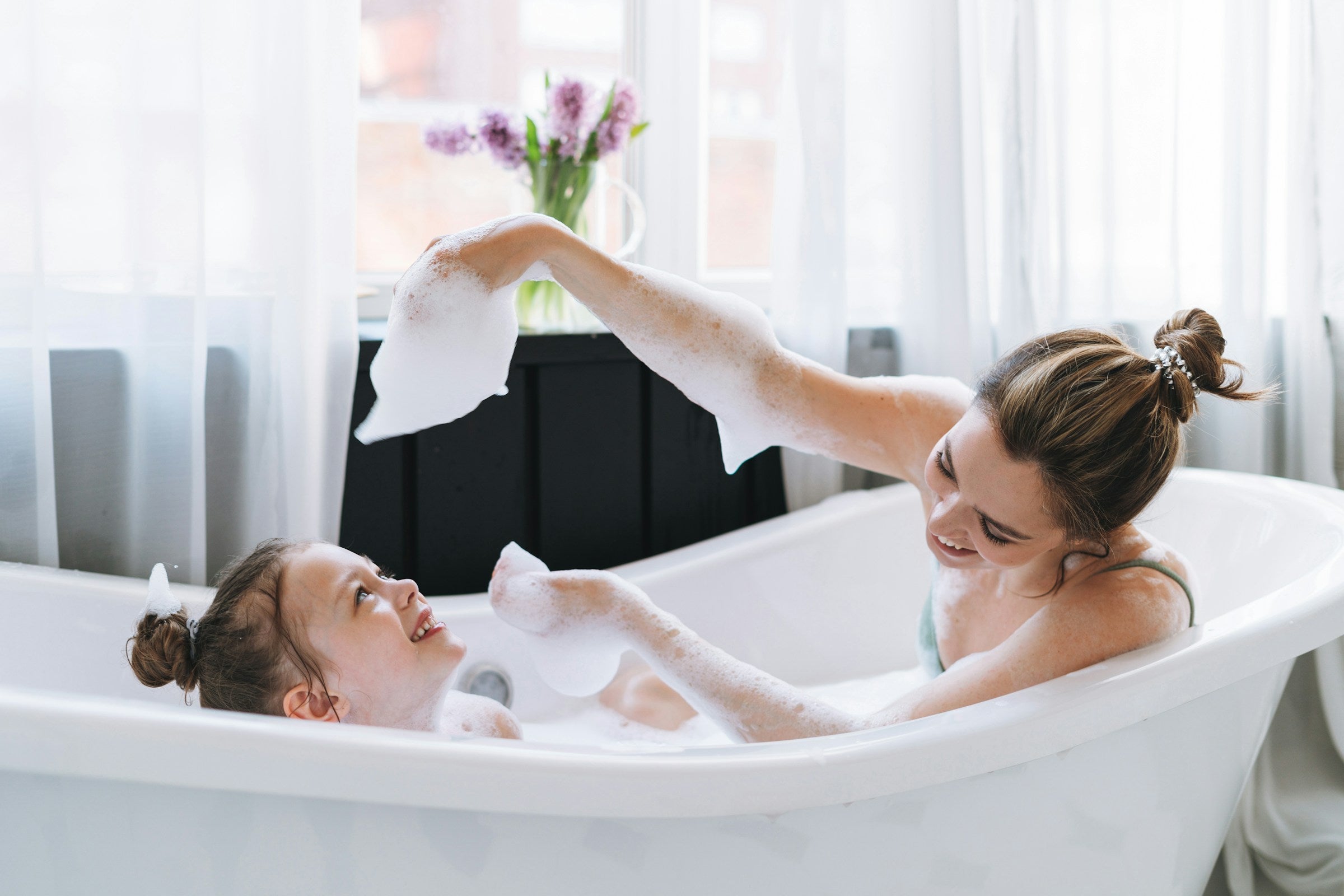 Woman and child in a bathtub with a towel and flowers in the background