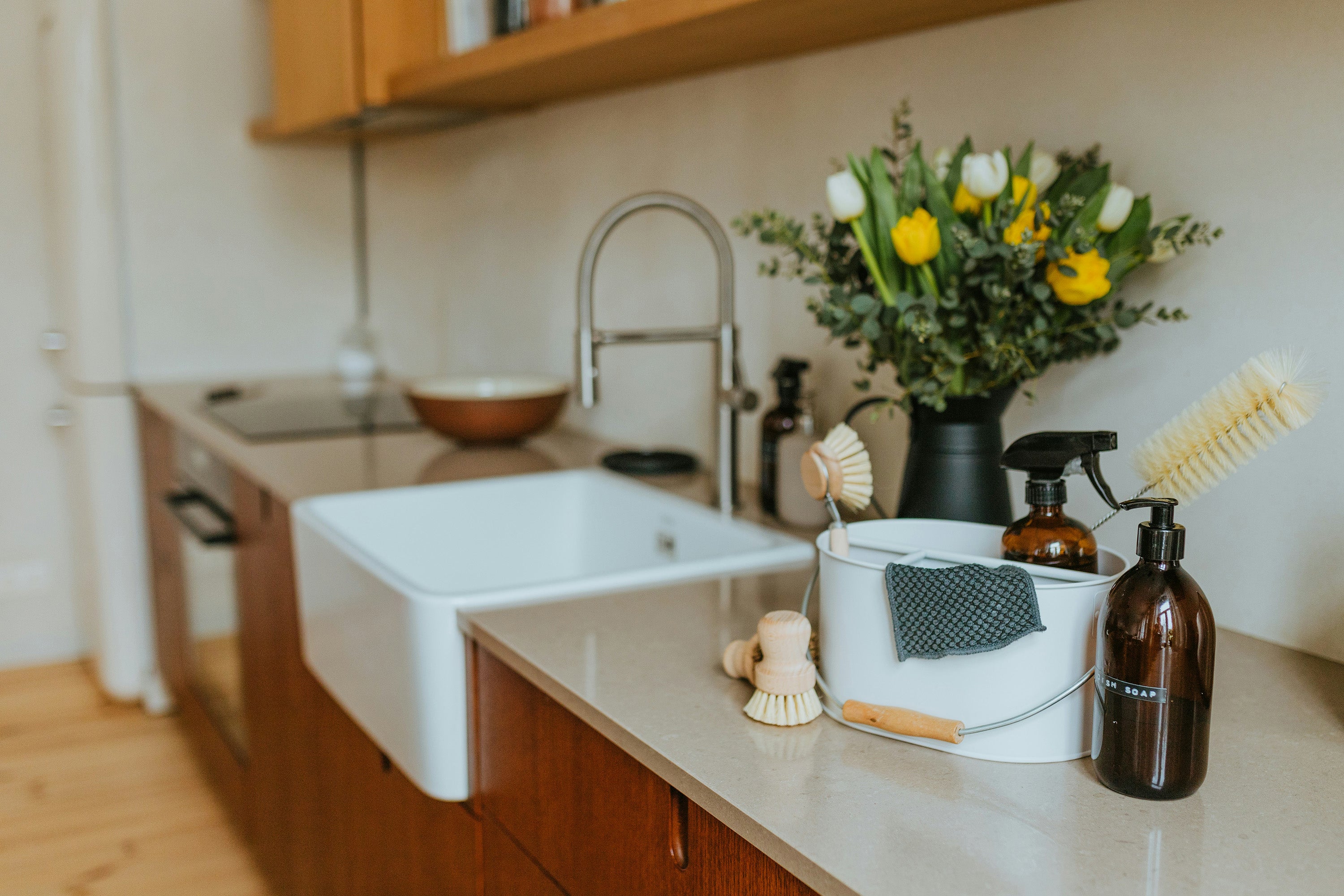Kitchen sink area with cleaning supplies and a flower arrangement on a countertop.